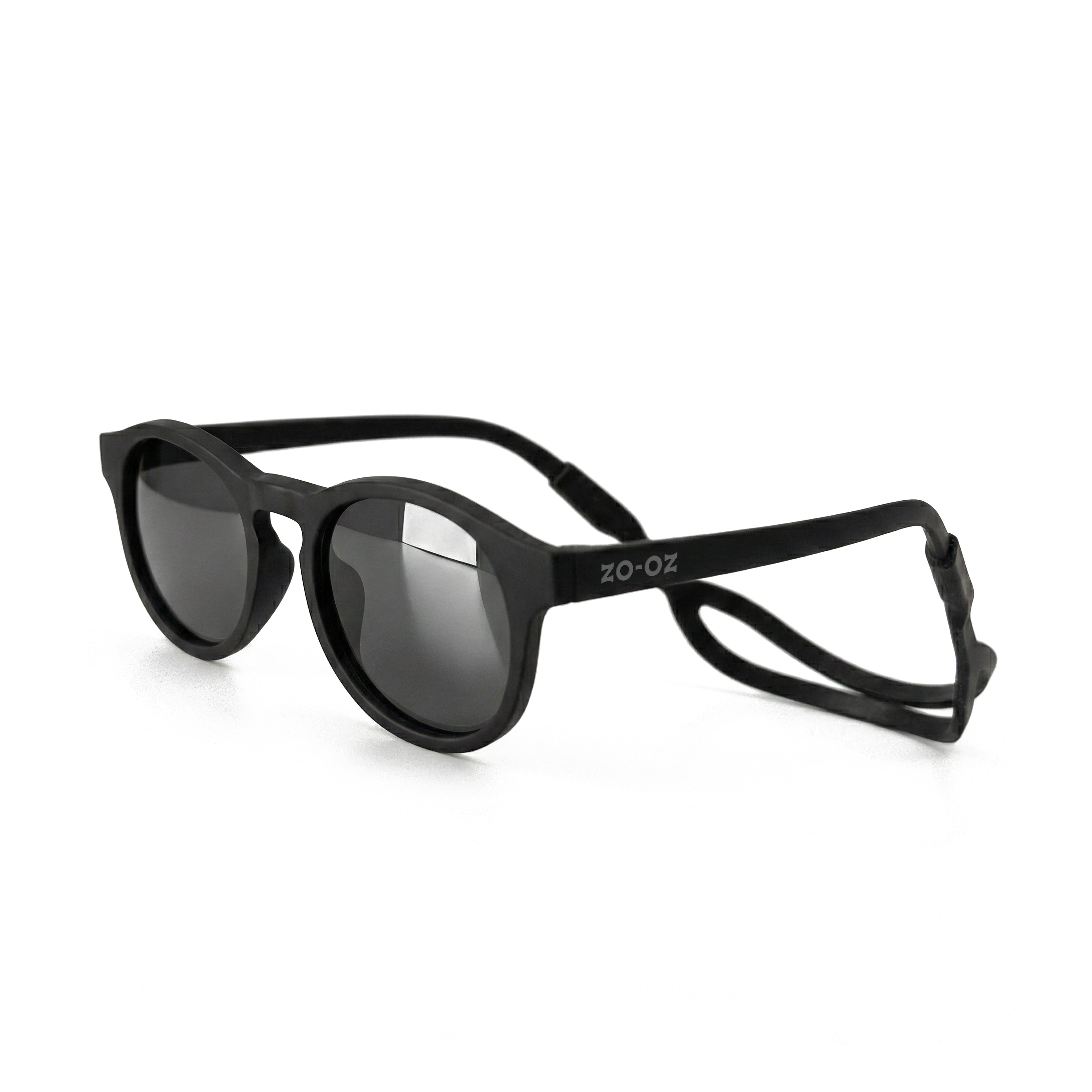 Occhiali da sole zo-oz stile pantos modello Pop nero opaco con fascetta nera per bambini 0-2 anni. Inquadratura laterale in prospettiva con le aste aperte appoggiate su una superficie.
